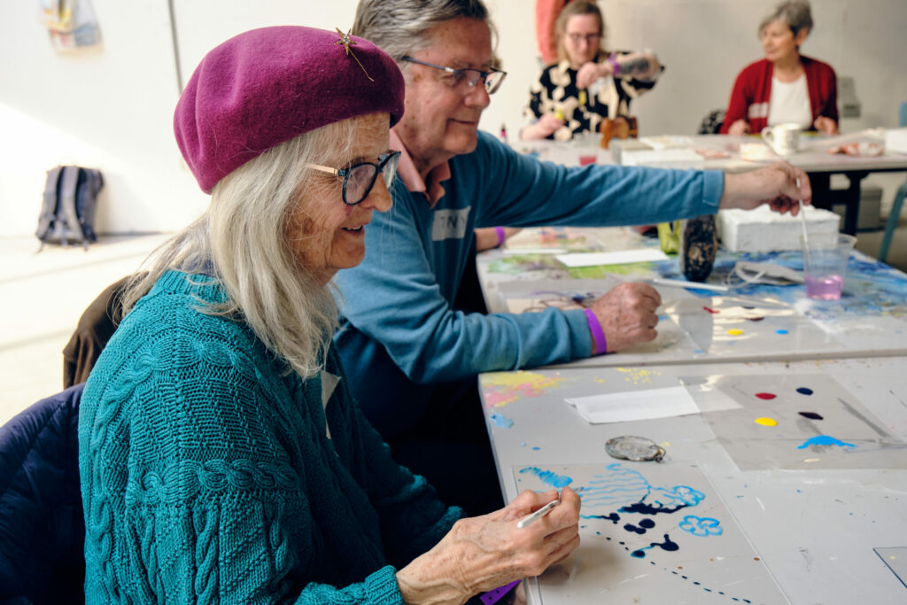 An older woman and an older man are painting on clear pieces of plastic.