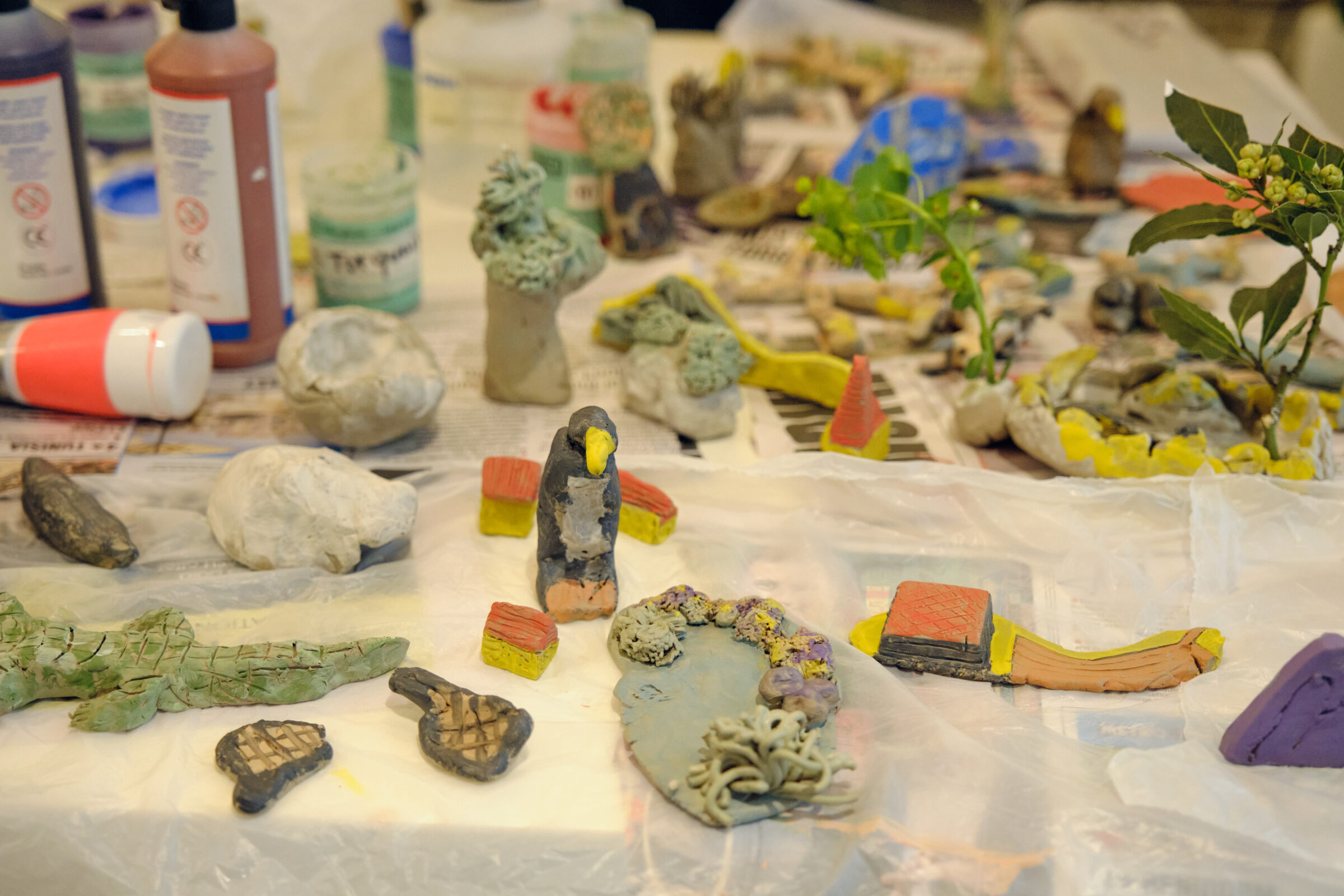 Lots of colourful clay pieces - including a penguin, a crocodile and plants, are on a table, alongside pots of glazes