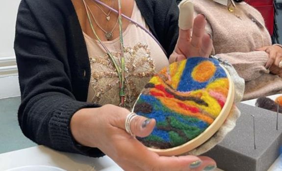 Bright coloured felting design being held by the participant that created it.