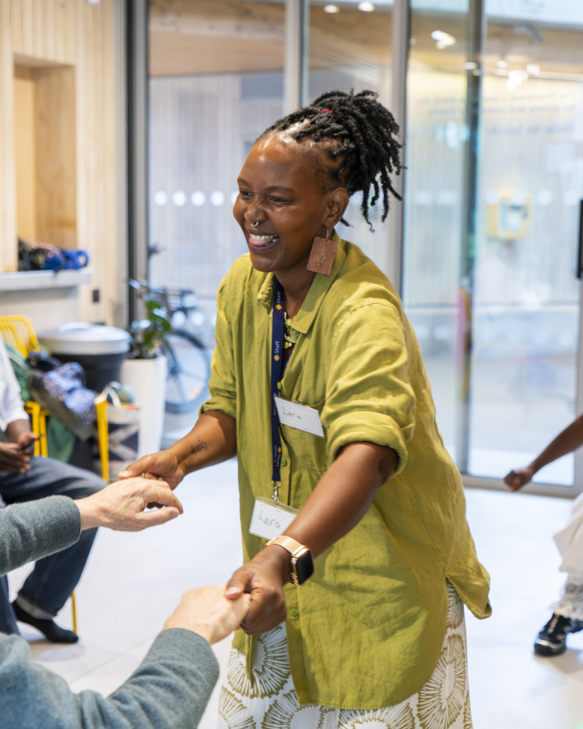 A smiling black woman is standing and holding both hands with a seated man